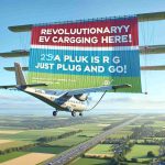 High-definition, realistic image of a flying message banner in the sky. The banner displays a message saying 'Revolutionary EV Charging is Here! Just Plug In and Go!'. The image should show a detailed clear sky with the colorful banner clearly visible, with a complementary contrast. The banner is being towed by a plane. Below, a hint of green fields and trees should be seen to accentuate the outdoor atmosphere.